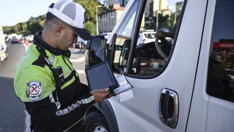 Yeşil üniforma giymiş bir trafik polisi, elindeki tabletle araç kontrolü yapıyor.