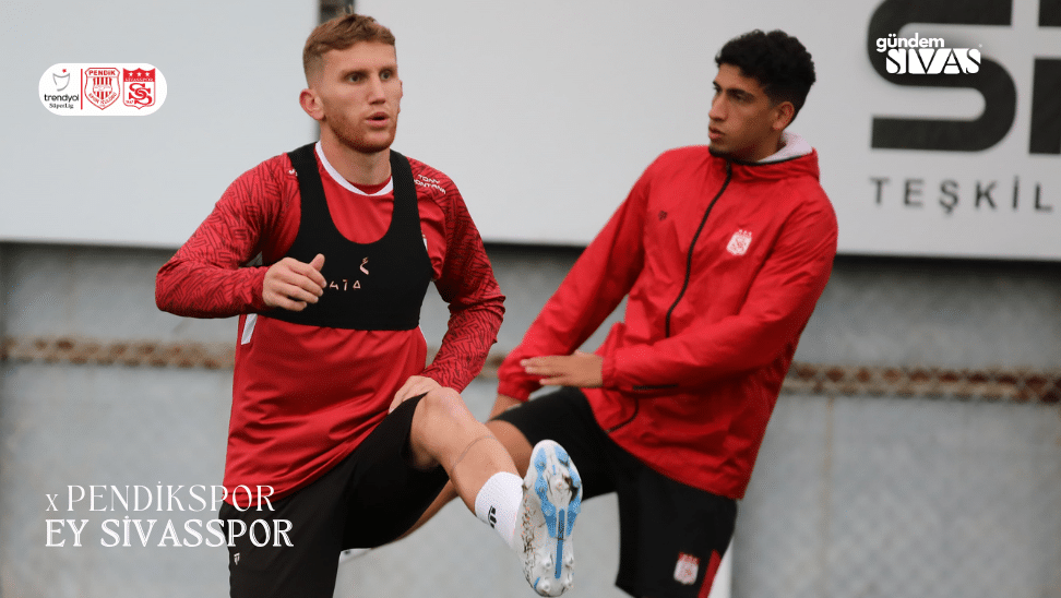 Antrenman yapan iki futbolcu, birinin bacaklarını kaldırarak ısınma hareketi yaptığı görülüyor.
