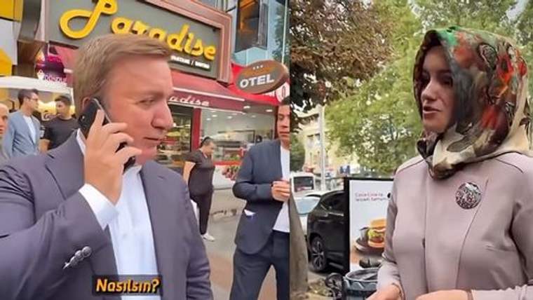 Sokakta telefonla konuşan bir adam ile başörtülü bir kadın, araçlar ve mağaza tabelaları önünde görülüyor.