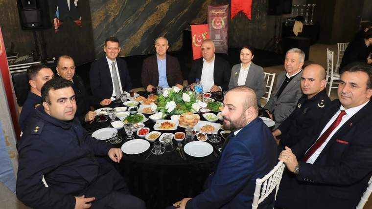 Kahvaltı sofrası etrafında takım elbiseli ve üniformalı kişilerin bulunduğu kalabalık bir grup oturuyor.