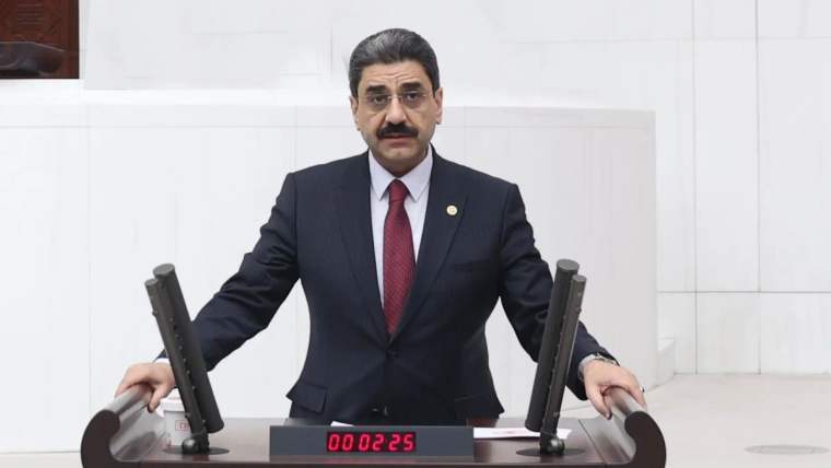 Kürsüde konuşan bir kişi, önünde mikrofonlar ve zaman sayacı var.