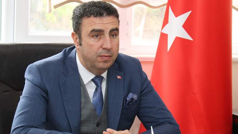 Takım elbiseli bir kişi, masasının başında otururken yanında Türk bayrağı görülüyor.
