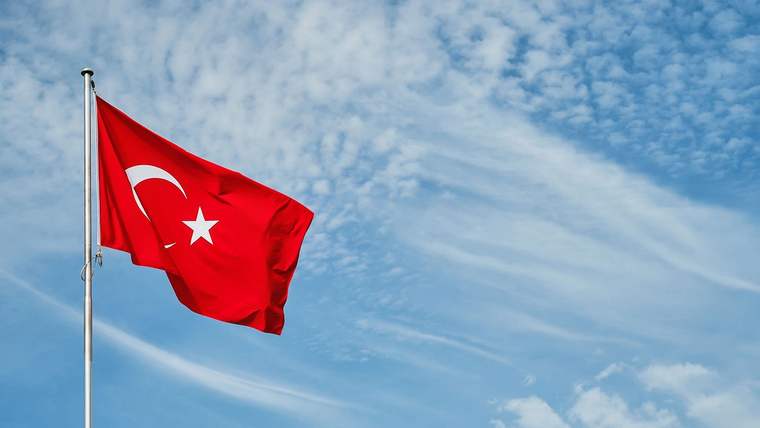 Mavi gökyüzü önünde, direğe asılı dalgalanan Türk bayrağı görülüyor.