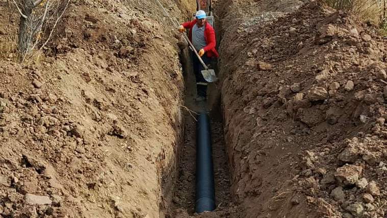 Toprağa açılmış bir hendekte, bir işçi siyah boru yerleştiriyor.