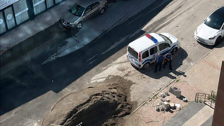 Bina önünde kırmızı ve mavi işaretli beyaz bir araç ile çevresinde duran birkaç kişi görülüyor.