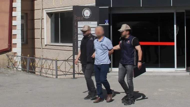 İki güvenlik görevlisi, bir kişiyi kolundan tutarak bir binanın önünde yürütüyor.