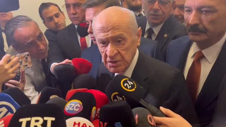 Bir grup gazetecinin çevresinde bulunan bir kişi, mikrofonlara cevap veriyor.