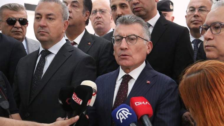 Bir grup insan, basın toplantısında mikrofonlar önünde duruyor; bir kişi konuşuyor.