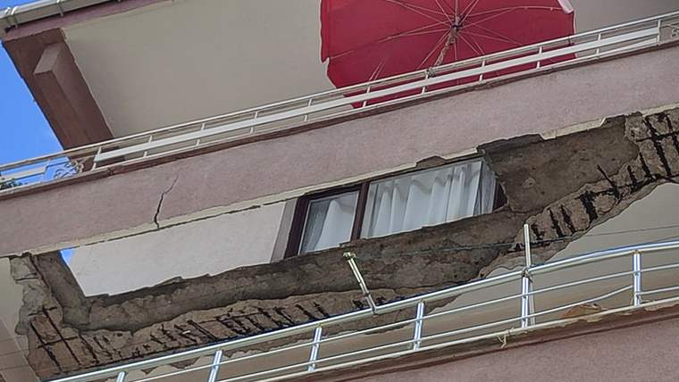 Beş katlı bir binanın balkonunun bir kısmı çökmüş, balkon demirleri görünmekte.