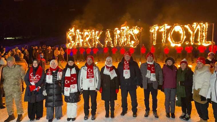 Karlı alanda, Türk bayraklı atkılar takan bir grup kişi önünde meşalelerle “SARIKAMIŞ” yazısı oluşturuluyor.