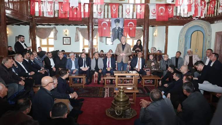 Bir grup insan, geleneksel bir mekanda oturmuş, bir kişi konuşma yapıyor.