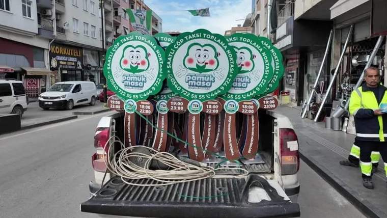 Kamyonetin açık kasasında yeşil yuvarlak tabelalar ve sarılı kablolar, şehir sokağında görülüyor.