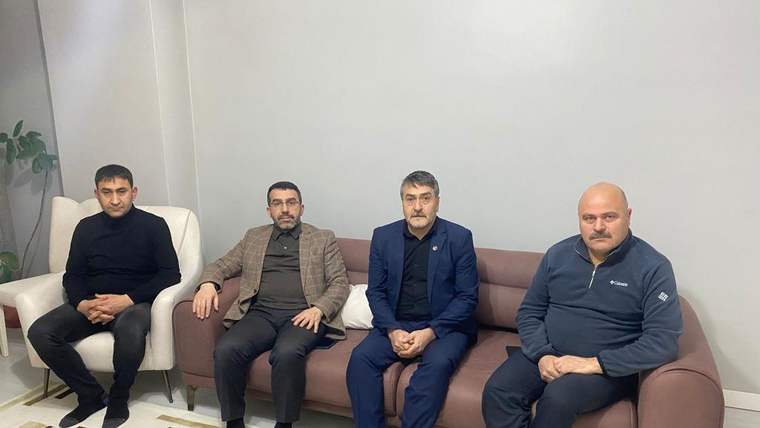 Bir odada koltuk ve sandalyelerde oturan dört erkek, kameraya doğru yan yana poz veriyor.