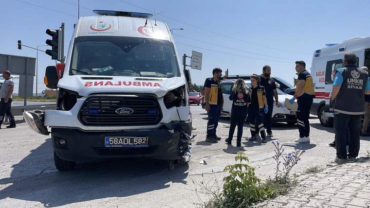 Ambulansın ön kısmında hasar var, çevresinde sağlık ekipleri ve bir kadın duruyor.