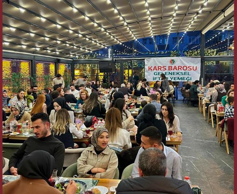 Üzerinde “Kars Barosu Geleneksel İftar Yemeği” yazan pankartın önünde kalabalık yemek salonunda oturuyor.