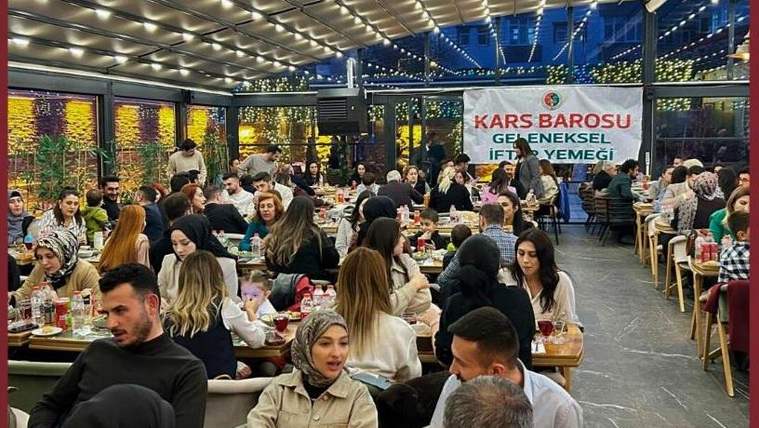 Üzerinde “Kars Barosu Geleneksel İftar Yemeği” yazan pankartın önünde kalabalık yemek salonunda oturuyor.