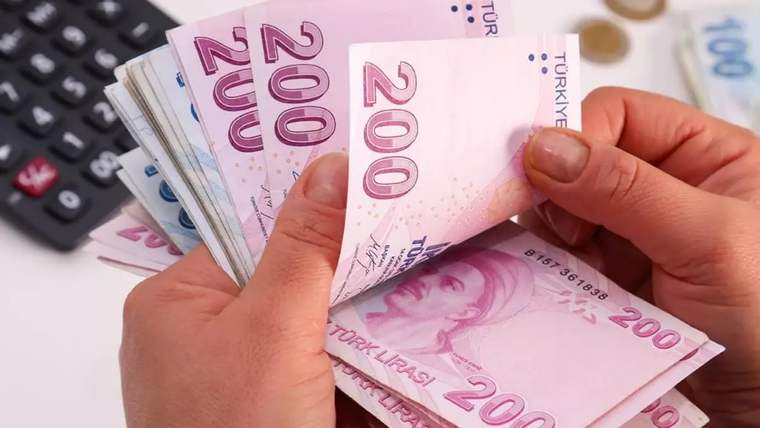 Bir kişinin elleri, 200 TL yazılı Türk lirası banknotlarını sayarken yanında hesap makinesi ve madeni paralar bulunuyor.