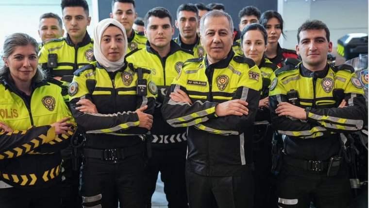 Sarı ve siyah üniformalı polisler, bir kişinin çevresinde kapalı alanda birlikte duruyor.