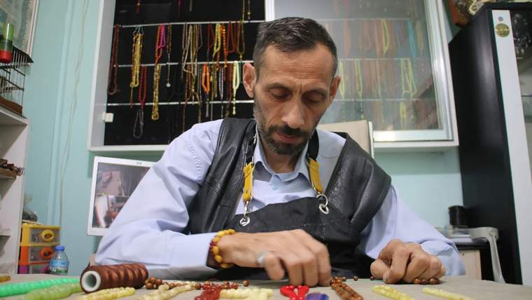 Tespih ustası, masanın üzerinde çeşitli tespih boncuklarıyla çalışıyor.