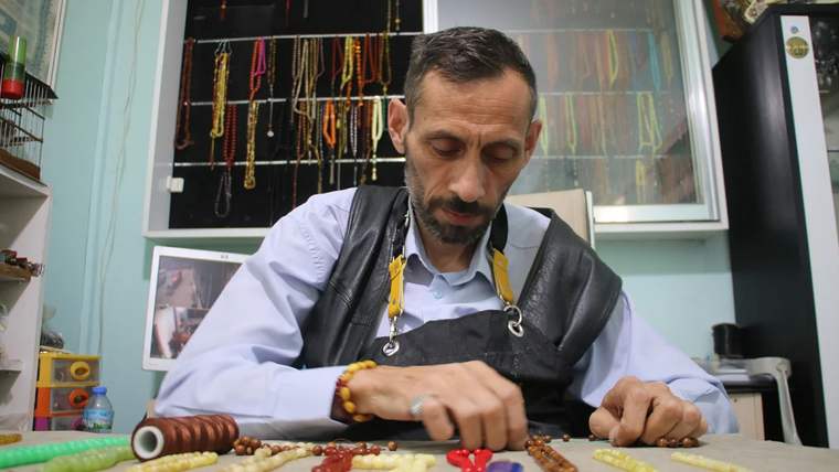 Tespih ustası, masanın üzerinde çeşitli tespih boncuklarıyla çalışıyor.