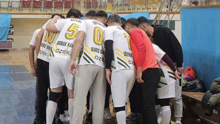 Salon içinde beyaz formalı voleybolcular, kırmızı tişörtlü bir kişiyle birlikte takım halinde kenetleniyor.