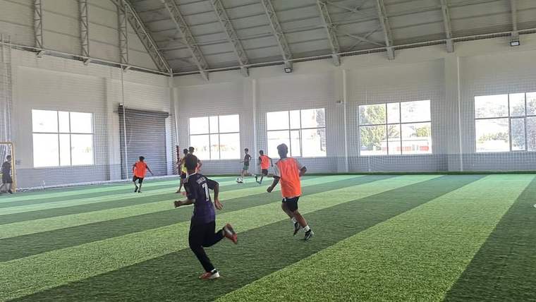 Futbol sahasında, turuncu ve mor tişörtlü çocuklar futbol oynuyor.