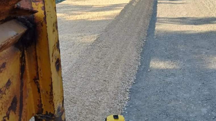 Asfalt serimi yapılan yolda, sarı iş makinesinin bir bölümü ve yol yüzeyindeki farklı kaplamalar görülüyor.
