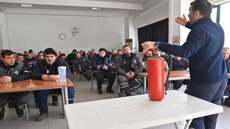Bir eğitim salonunda, yangın eğitimi veren bir kişi, masanın üzerinde yangın söndürücü tutuyor.