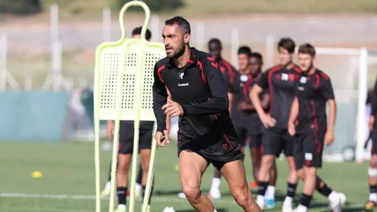 Antrenman sahasında, siyah şort ve tişört giymiş bir futbolcu, önünde antrenman seti ile koşuyor.