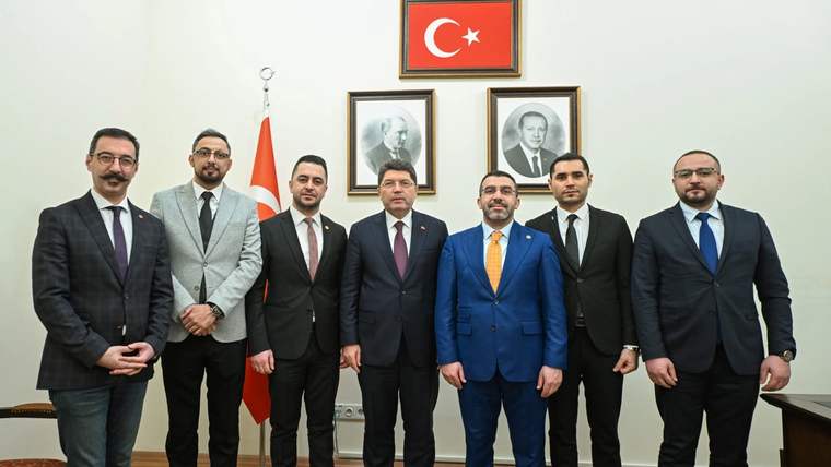 Türk bayrağı ve iki portre önünde, takım elbiseli altı kişi bir odada yan yana duruyor.