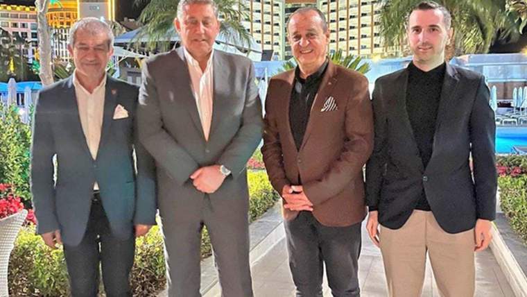Palmiye ağaçları ve ışıklı binalar önünde duran dört erkek, açık havada birlikte poz veriyor.