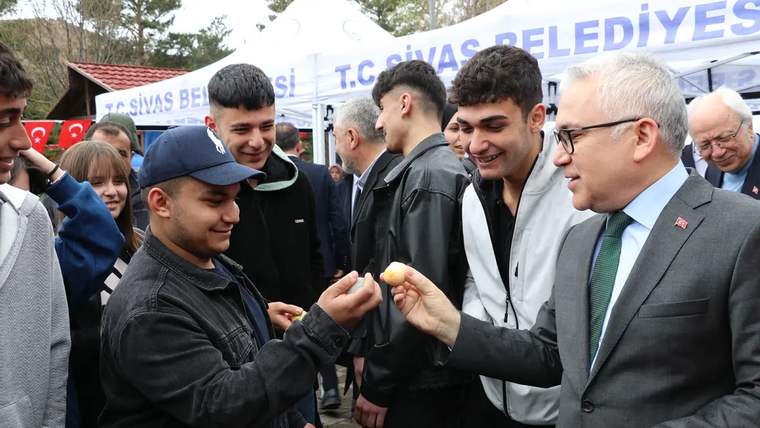 Bir grup genç, bir kişiye yumurta uzatıyor; arka planda Sivas Belediyesi standı görünüyor.
