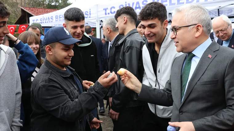 Bir grup genç, bir kişiye yumurta uzatıyor; arka planda Sivas Belediyesi standı görünüyor.