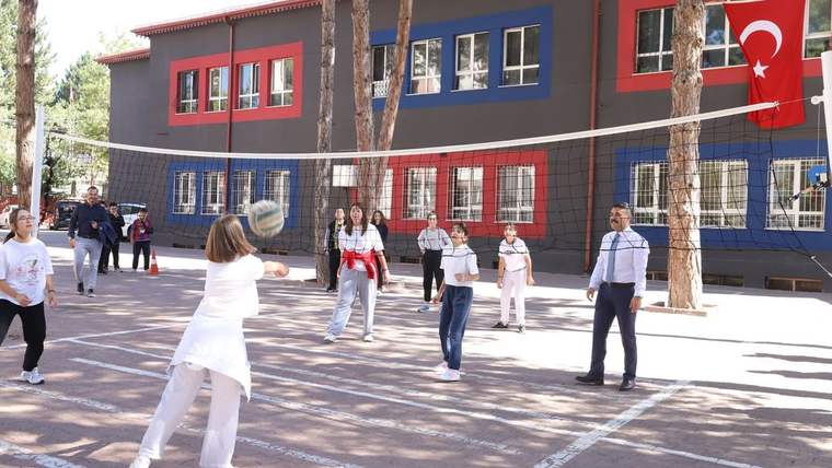 Bir grup öğrenci voleybol oynarken, arka planda Ziya Gökalp Ortaokulu ve Türk bayrağı görünmekte.