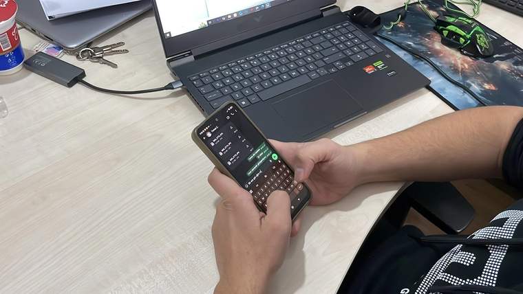 Bir kişinin akıllı telefonla mesaj yazdığı, masada dizüstü bilgisayar ve anahtarların bulunduğu bir görüntü.