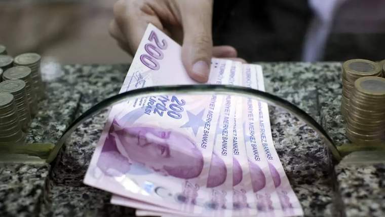 Bir kişinin elinde 200 TL banknotlar, bir masanın üzerinde yer alan bozuk paralarla birlikte görünüyor.