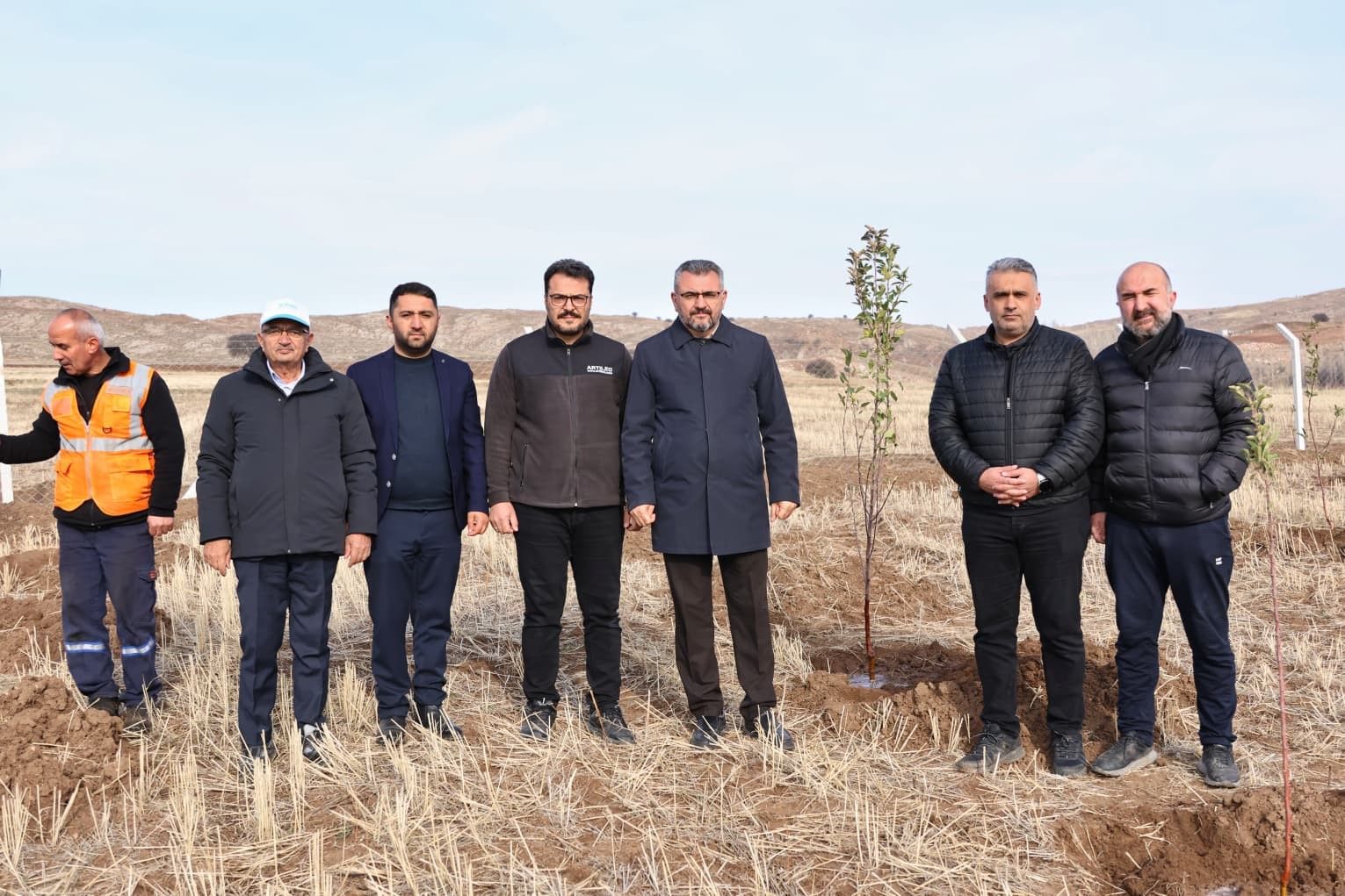 Sivas OSB'de ağaç diken bir grup insan, arka planda kurak bir arazi görünmekte.