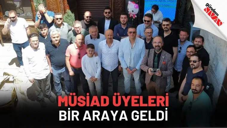 Bir bina girişinin önünde, çoğu erkeklerden oluşan kalabalık bir grup birlikte duruyor.