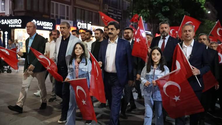 Türk bayrakları taşıyan kalabalık bir grup, sokakta yürüyerek ilerliyor.