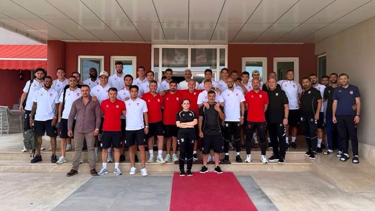 Bir bina girişinde, kırmızı halı üzerinde ve çevresinde duran spor giyimli kalabalık grup poz veriyor.