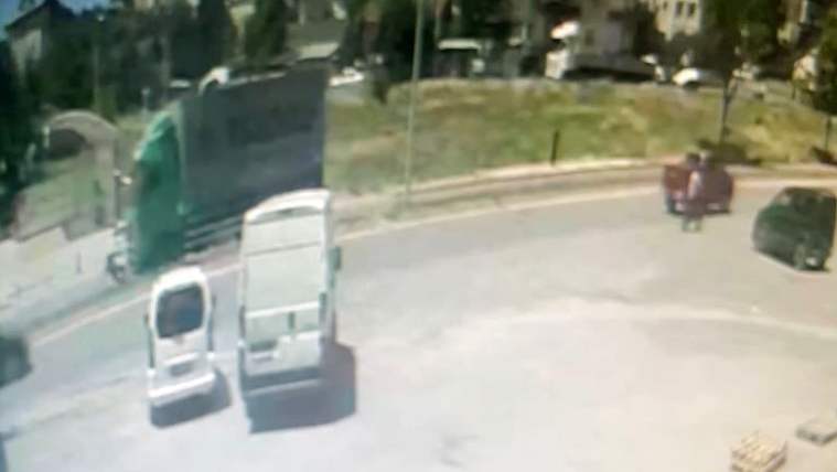 Bir kamyon ve birkaç araç, bir otoparkta duruyor. Arka planda yeşil bir alan görünmekte.