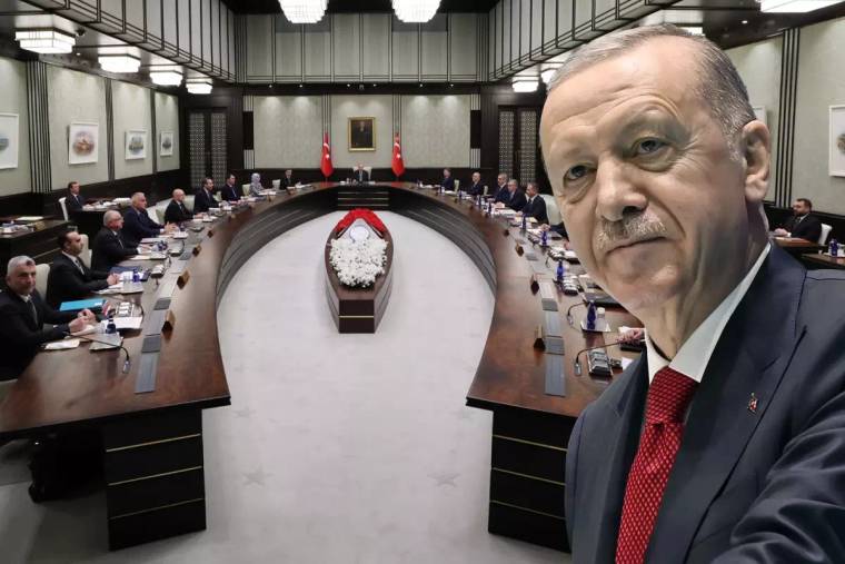 U biçimli masaların çevresinde oturan kişiler, salonda iki Türk bayrağı ve önde takım elbiseli bir kişi görülüyor.