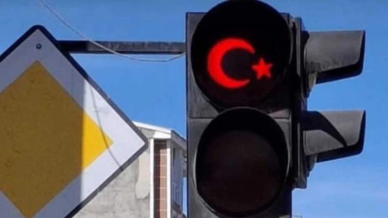 Trafik lambasının kırmızı ışığında ay yıldızlı Türk bayrağı sembolü, yanında yön levhasıyla görülüyor.