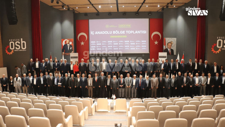 Bir salonda, birçok kişi grup halinde poz veriyor; arka planda Türk bayrağı ve Atatürk portresi var.