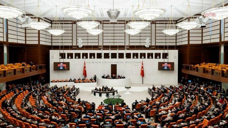 Türkiye Büyük Millet Meclisi Genel Kurul salonunda çok sayıda kişi sıralarda otururken kürsü bölümü görülüyor.