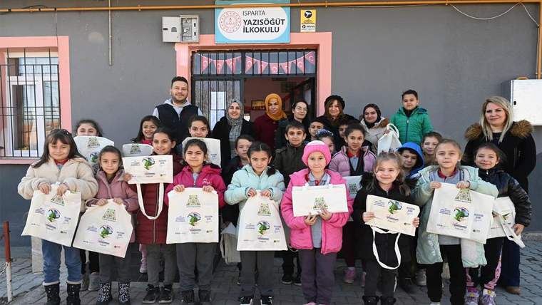Isparta Yazısöğüt İlkokulu önünde çocuklar, ellerinde belgeler ve bez çantalarla poz veriyor.