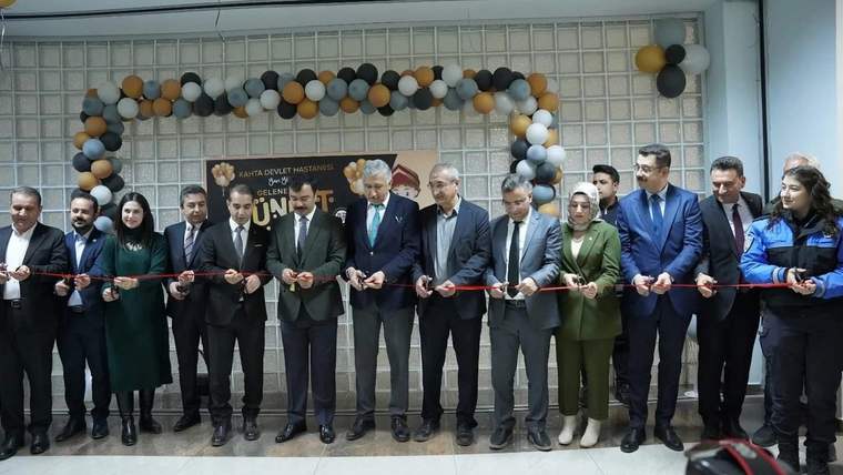 Balonlarla süslenmiş giriş önünde, kurdele kesen takım elbiseli ve üniformalı kişiler yan yana duruyor.