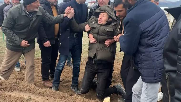 Bir grup insan, bir mezarın etrafında toplanmış, bir kişi diz çökerek ağlıyor.