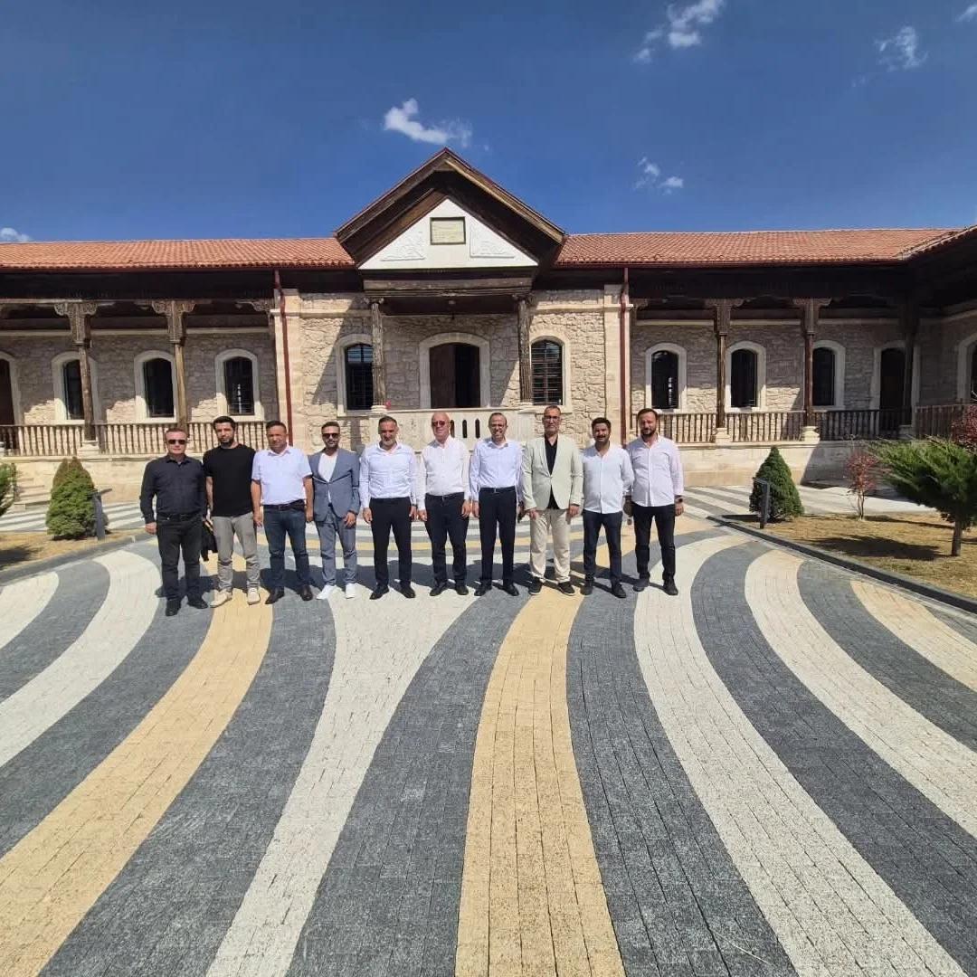 Kütüphane binasının önünde, çeşitli kişiler bir arada duruyor. Arka planda tarihi bir yapı görünmekte.