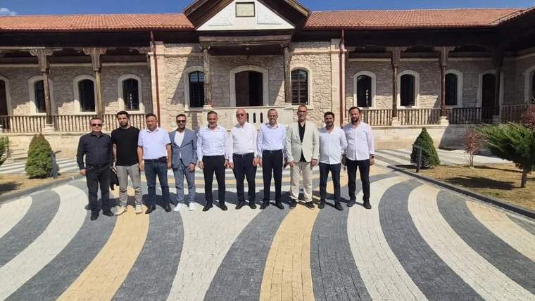 Kütüphane binasının önünde, çeşitli kişiler bir arada duruyor. Arka planda tarihi bir yapı görünmekte.